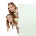 Two little girls peeking out from behind a white advertising ban Royalty Free Stock Photo