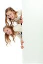 Two little girls peeking out from behind a white advertising ban Royalty Free Stock Photo