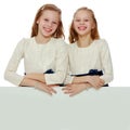 Two little girls peeking out from behind a white advertising ban Royalty Free Stock Photo