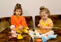 Two little girls play with dolls on a sofa