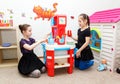 Two little girls play role game with toy kitchen in day care