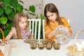 Two little girls pour water into glasses with paint to decorate eggs.