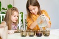 Two little girls pour water into glasses with paint to decorate eggs.