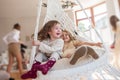 Two little girls ride on a macrame swing at home near the Christmas tree. Sisters have fun