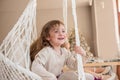 Two little girls ride on a macrame swing at home near the Christmas tree. Sisters have fun