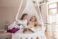 Two little girls ride on a macrame swing at home near the Christmas tree. Sisters have fun