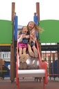 Two little girls roll down the slide on playground laughing merrily and closing their eyes in fear.