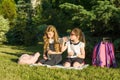 Two little girls schoolchildren drink water from bottle on sunny day, sitting in the park Royalty Free Stock Photo