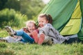 Two little girls sisters sitting on the green grass next to camping tent entrance, cheerfully laughing about jokes they told to Royalty Free Stock Photo