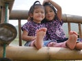 Two little girls, sisters, 2 and 3 years old, smiling and making a heart shape on a bamboo bench near a lake - sisters bond & love