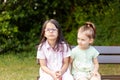 Two little girls sitting on a bench in the park and looking at each other Royalty Free Stock Photo