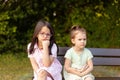 Two little girls sitting on a park bench and looking at each other Royalty Free Stock Photo