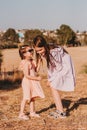 Two little girls wearing eco style dresses walking together in summer field with dry grass and sharing secrets. Kids having fun in Royalty Free Stock Photo