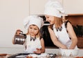 Two little girls in white chef hats play fun in the kitchen. Children cook food Royalty Free Stock Photo