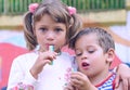 Two little happy kids boy and girl stand in each other`s arms and chewing gum. Siblings on playground in summer or spring in Royalty Free Stock Photo