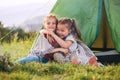 Two little hugging girls sisters sitting on the green grass next camp tent entrance, cheerfully smiling. Careless childhood,