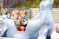 Two little kid boys on carousel in amusement park