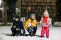 Two little kid boys and cute toddler girl sitting together playing with snow on winter night. Siblings, brothers and Royalty Free Stock Photo