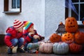 Two little kid boys sitting with traditional jack-o-lanterns pumpkins for halloween by the decorated scary door