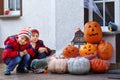 Two little kid boys sitting with traditional jack-o-lanterns pumpkins for halloween by the decorated scary door