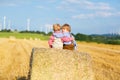 Two little kid boys, twins and siblings sitting on warm summer day on hay stack in wheat field. Happy children playing