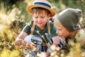 Two little kids with backpacks examining plants through magnifying glass in forest Royalty Free Stock Photo