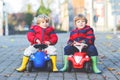 Two little kids boys in colorful clothes and rain boots driving toy cars. Best friends making competition, outdoors Royalty Free Stock Photo