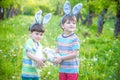 Two little kids boys and friends in Easter bunny ears during traditional egg hunt in spring garden, outdoors. Siblings having fun Royalty Free Stock Photo