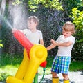 Two little kids boys playing with a garden hose sprinkler on hot and sunny summer day. Children having fun with Royalty Free Stock Photo