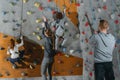 Two little kids climbing a wall at gym and their mother and father holding