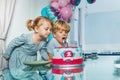 Two little kids girl and a boy blow candles on the birthday cake