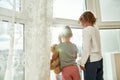 Two little kids in home clothes holding hands, looking out of a large window while spending time together at home Royalty Free Stock Photo