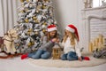 Two little pretty girls in red Christmas caps are sitting near t Royalty Free Stock Photo