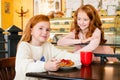 Two little red-haired sisters in coffee shop. One girl eats a cake, another came up to her and stares at her Royalty Free Stock Photo