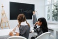 Two little schoolgirls sitting behind a desk, looking in a coorful book.