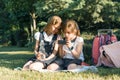 Two little schoolgirls using a smartphone. Children playing, reading, looking at the phone, in the park, golden hour. People,