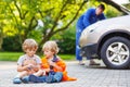 Two little sibling boys in orange safety vest during their father repairing family car Royalty Free Stock Photo