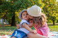 Two little siblings sitting on picnic blanket in park, sister kisses little brother on cheek Royalty Free Stock Photo