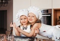 Two little sisters cuddle in the kitchen in white chef hats. Hilarious girlfriends play in the kitchen Royalty Free Stock Photo