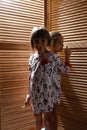 Two little sisters dressed in the pajamas are hiding in the closet with wooden doors