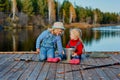 Two little sisters or friends sit with fishing rods on a wooden pier. They caught a fish and put it in a bucket. They are happy Royalty Free Stock Photo