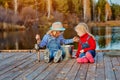 Two little sisters or friends sit with fishing rods on a wooden pier. They caught a fish and put it in a bucket. They are happy Royalty Free Stock Photo