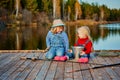 Two little sisters or friends sit with fishing rods on a wooden pier. They caught a fish and put it in a bucket. They are happy Royalty Free Stock Photo