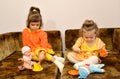 Two little sisters play with dolls on a sofa Royalty Free Stock Photo