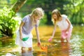 Two little sisters playing with paper boats by a river on warm and sunny summer day. Children having fun by the water. Royalty Free Stock Photo