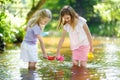 Two little sisters playing with paper boats by a river on warm and sunny summer day. Children having fun by the water. Royalty Free Stock Photo