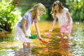 Two little sisters playing with paper boats by a river on warm and sunny summer day. Children having fun by the water. Royalty Free Stock Photo