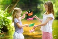 Two little sisters playing with paper boats by a river on warm and sunny summer day. Children having fun by the water. Royalty Free Stock Photo