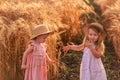 Two little sisters in straw hats and pink dresses are running around in a wheat field, having fun Royalty Free Stock Photo