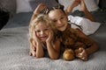 Two little sisters in white dresses laying at bed at daylight with bear toy. Family unity concept. Royalty Free Stock Photo